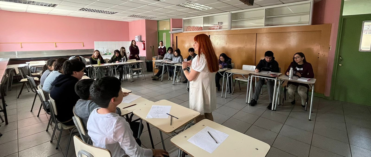 Fotografía de Sandra Garai dirigiéndose a estudiantes de educación básica que están reunidos en una media luna